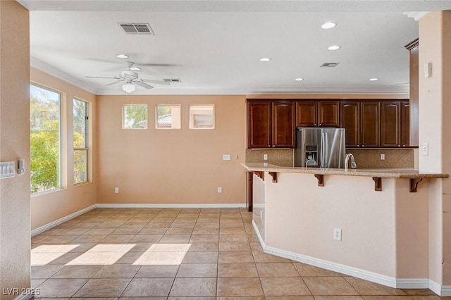 kitchen featuring decorative backsplash, stainless steel fridge, ornamental molding, a kitchen bar, and kitchen peninsula