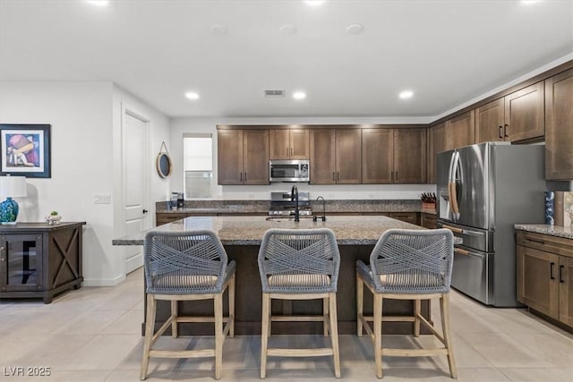 kitchen featuring an island with sink, appliances with stainless steel finishes, and dark stone counters