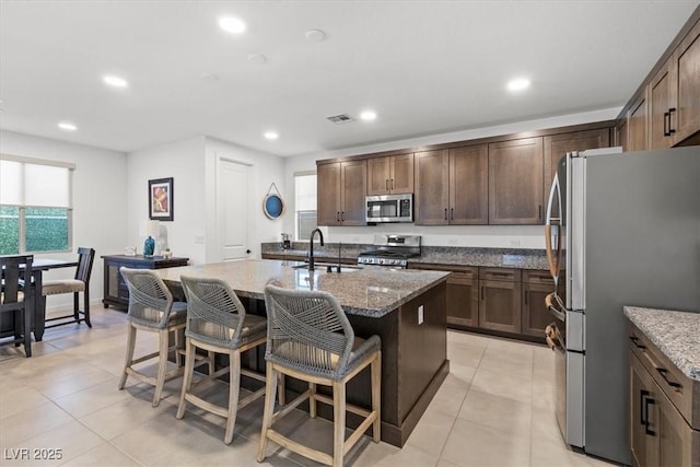 kitchen featuring light stone countertops, appliances with stainless steel finishes, a kitchen bar, a kitchen island with sink, and sink