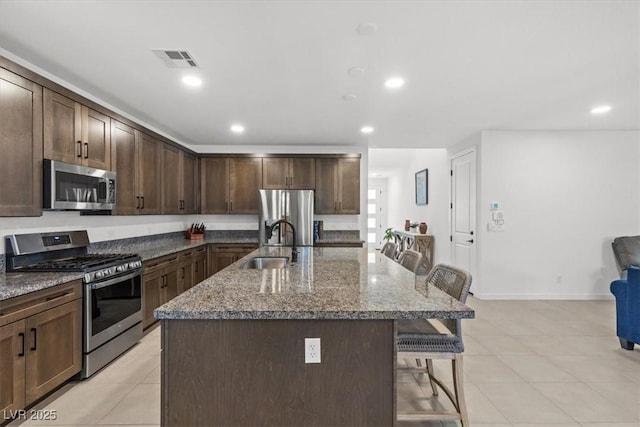 kitchen with dark brown cabinetry, a breakfast bar, an island with sink, and stainless steel appliances