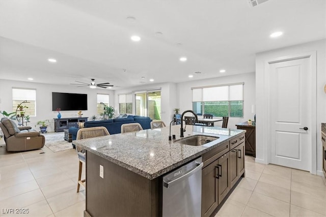 kitchen with light stone counters, stainless steel dishwasher, ceiling fan, sink, and a center island with sink