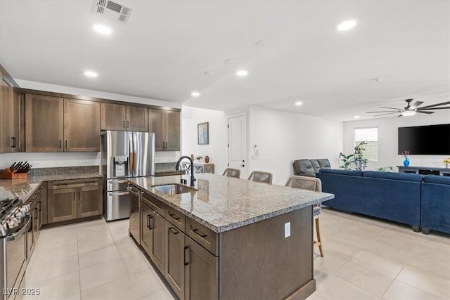 kitchen featuring a breakfast bar, sink, ceiling fan, light stone counters, and stainless steel appliances