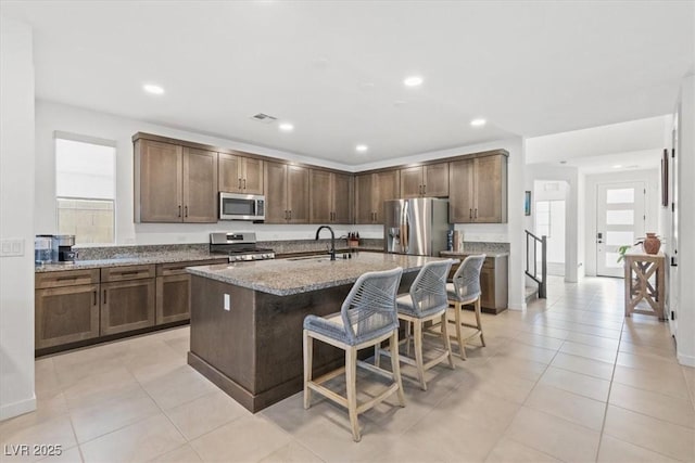 kitchen with a kitchen island with sink, a breakfast bar, stainless steel appliances, and light stone counters