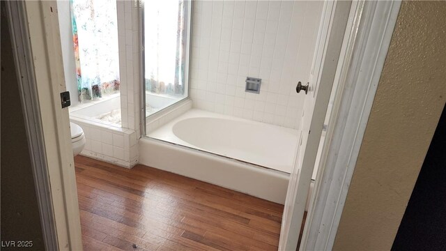 bathroom with hardwood / wood-style floors, toilet, and tiled tub