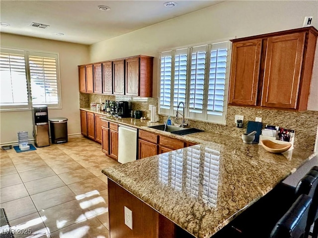 kitchen with sink, stainless steel dishwasher, light stone countertops, light tile patterned flooring, and kitchen peninsula