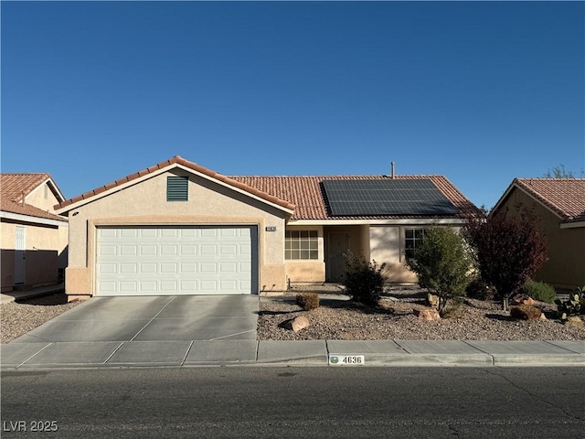 ranch-style house featuring an attached garage, solar panels, a tiled roof, driveway, and stucco siding