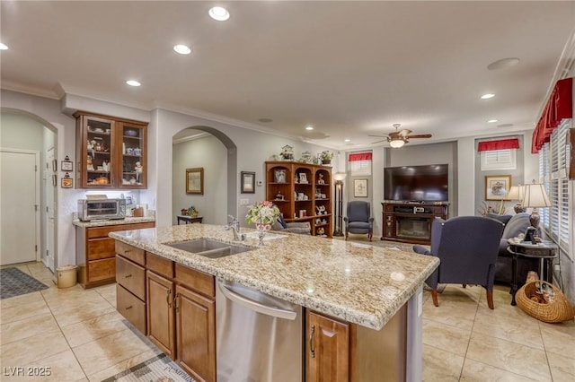 kitchen with stainless steel dishwasher, light stone counters, a kitchen island with sink, sink, and a fireplace