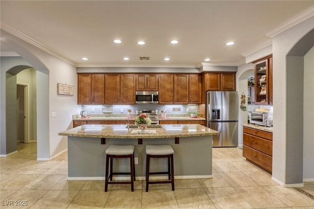 kitchen with appliances with stainless steel finishes, a center island with sink, light stone counters, and a breakfast bar area