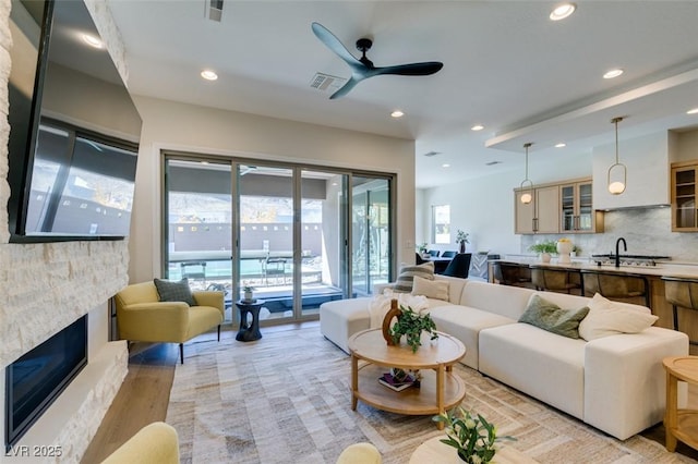 living room with a stone fireplace, ceiling fan, and light hardwood / wood-style flooring