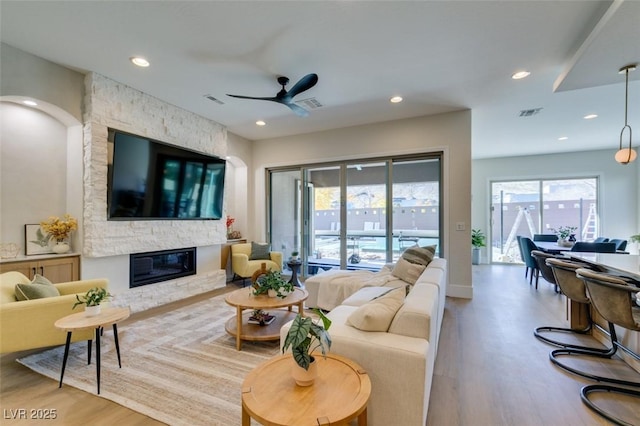 living room featuring ceiling fan, a stone fireplace, and wood-type flooring