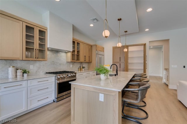 kitchen featuring light stone countertops, backsplash, a center island with sink, stainless steel stove, and a breakfast bar area