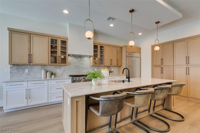 kitchen with sink, a kitchen island with sink, tasteful backsplash, light stone counters, and high quality appliances