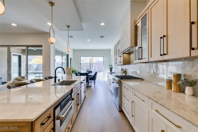 kitchen with sink, high end stainless steel range oven, light stone counters, decorative light fixtures, and decorative backsplash