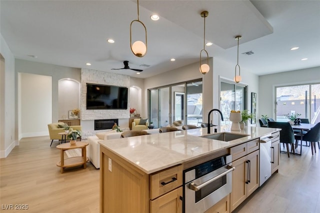 kitchen with ceiling fan, light stone countertops, sink, decorative light fixtures, and a center island with sink