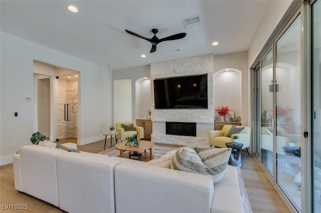 living room featuring ceiling fan, a fireplace, and light wood-type flooring