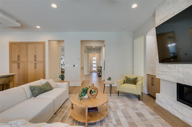 living room with a stone fireplace and light wood-type flooring