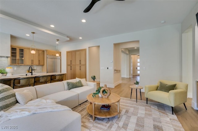 living room with ceiling fan, sink, and light wood-type flooring