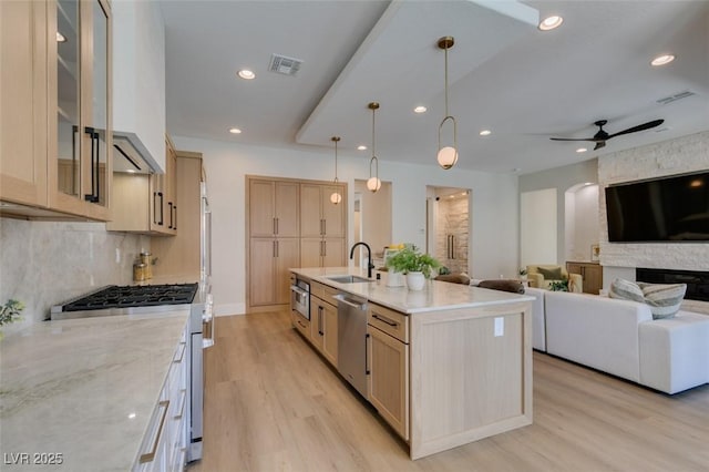 kitchen featuring a kitchen island with sink, ceiling fan, light brown cabinetry, light hardwood / wood-style floors, and stainless steel appliances