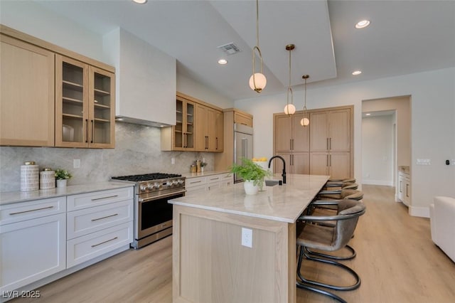 kitchen with high end range, a kitchen breakfast bar, light stone countertops, a center island with sink, and white cabinetry