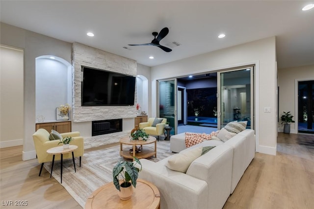 living room with light hardwood / wood-style flooring, ceiling fan, and a stone fireplace