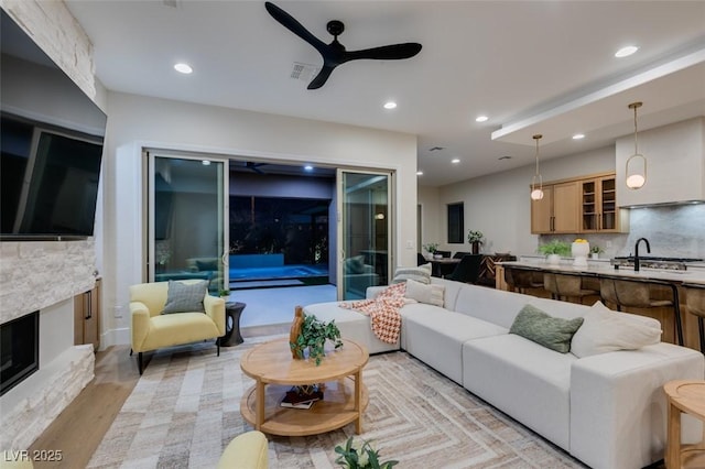 living room featuring ceiling fan, a fireplace, sink, and light hardwood / wood-style flooring