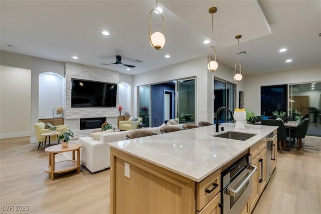 kitchen featuring light stone counters, an island with sink, pendant lighting, and ceiling fan