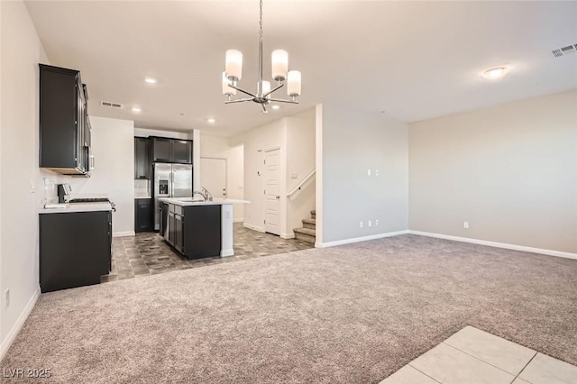 kitchen featuring stove, a kitchen island with sink, hanging light fixtures, a notable chandelier, and light colored carpet