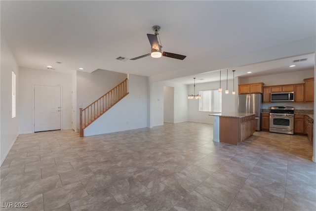 kitchen featuring appliances with stainless steel finishes, light stone counters, ceiling fan with notable chandelier, a center island, and hanging light fixtures