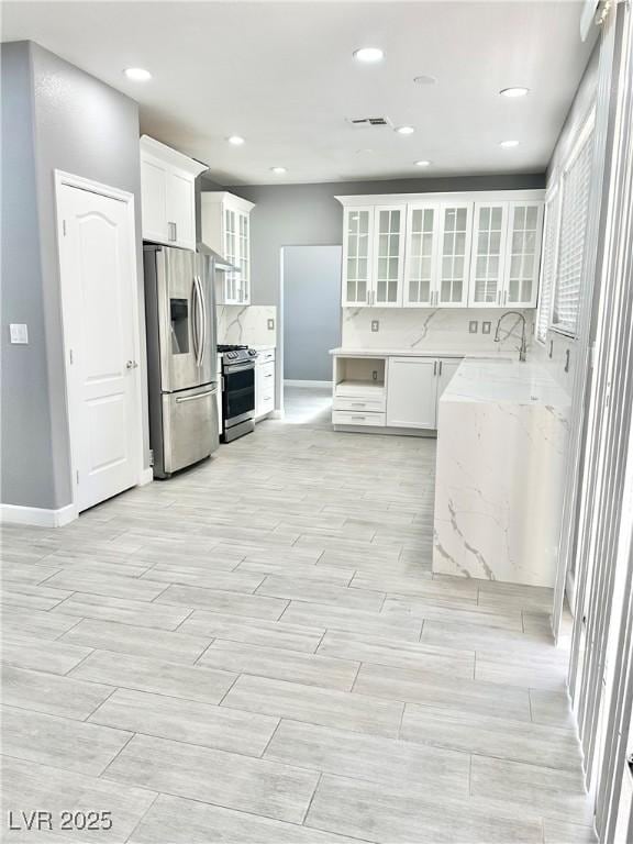 kitchen featuring sink, light stone countertops, appliances with stainless steel finishes, tasteful backsplash, and white cabinetry