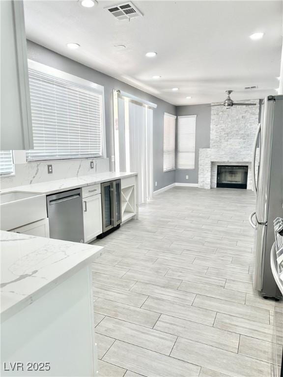 kitchen with light stone countertops, appliances with stainless steel finishes, beverage cooler, a fireplace, and white cabinetry