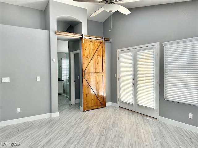 spare room featuring a barn door, high vaulted ceiling, light hardwood / wood-style flooring, and ceiling fan