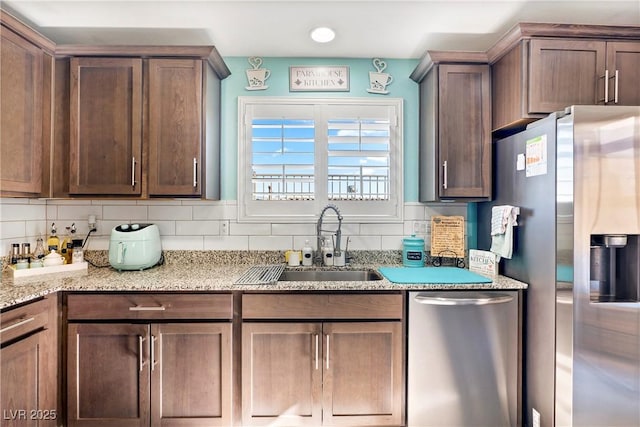 kitchen featuring backsplash, light stone countertops, sink, and stainless steel appliances