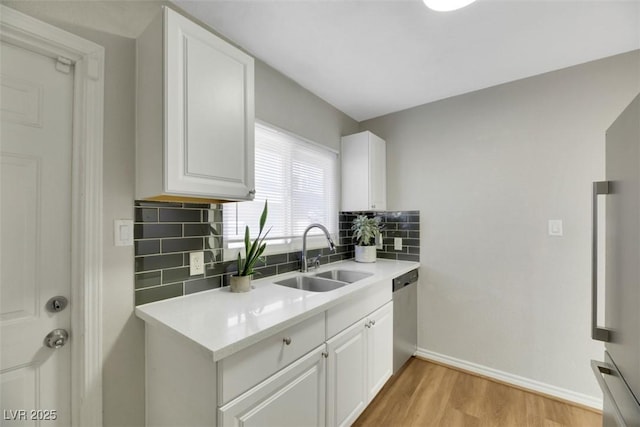 kitchen with sink, tasteful backsplash, stainless steel dishwasher, white cabinets, and light wood-type flooring