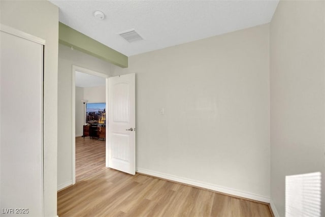 empty room with a textured ceiling and light hardwood / wood-style flooring