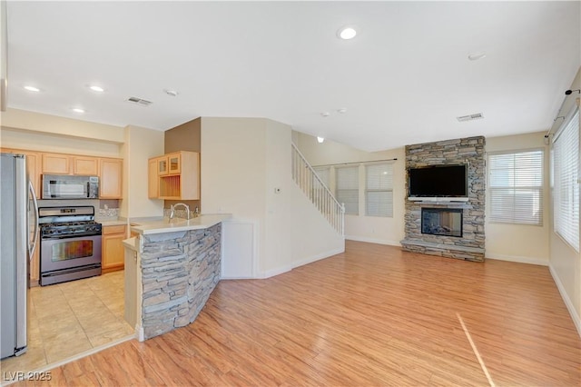 kitchen featuring light wood-type flooring, a fireplace, stainless steel appliances, and light brown cabinets