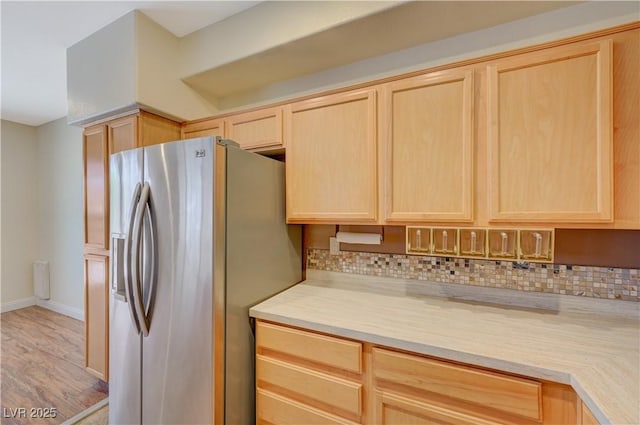 kitchen featuring stainless steel refrigerator with ice dispenser, light wood-type flooring, decorative backsplash, and light brown cabinets