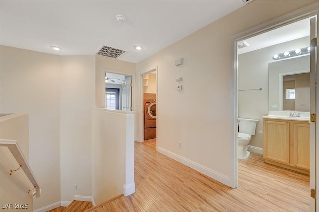 hall with washer / clothes dryer, sink, and light wood-type flooring