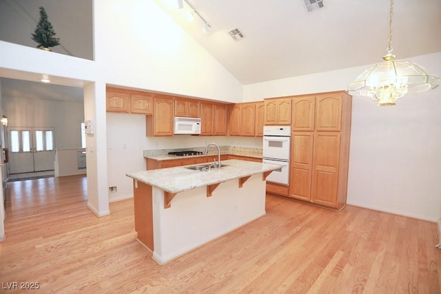 kitchen with an island with sink, white appliances, light wood-type flooring, high vaulted ceiling, and pendant lighting