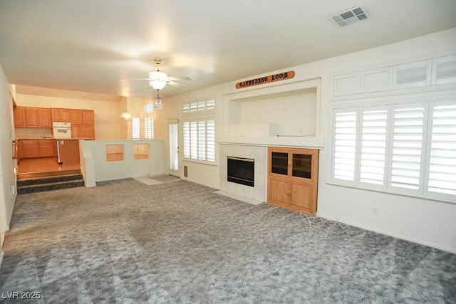 unfurnished living room with ceiling fan, a fireplace, and dark colored carpet