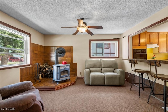 carpeted living room featuring ceiling fan, a wood stove, and a textured ceiling