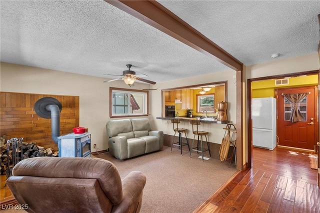 living room with a textured ceiling, ceiling fan, a wood stove, and sink