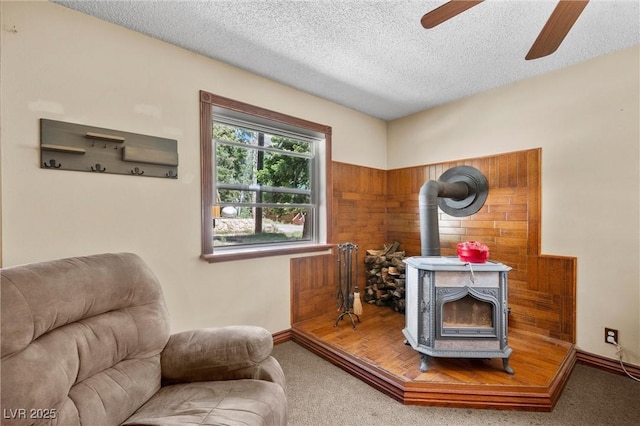 living area featuring a wood stove, ceiling fan, carpet floors, and a textured ceiling