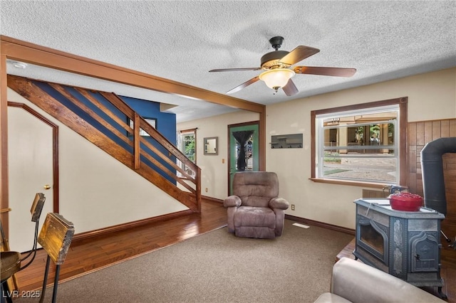 living room featuring a wood stove, ceiling fan, wood-type flooring, and a textured ceiling