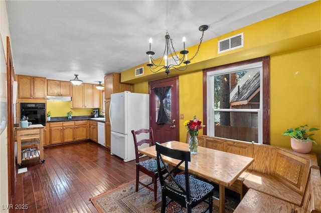 kitchen featuring dark wood-type flooring, an inviting chandelier, decorative light fixtures, white appliances, and light brown cabinetry