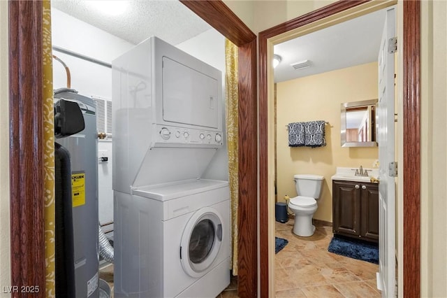 clothes washing area with a textured ceiling, water heater, sink, and stacked washer and clothes dryer