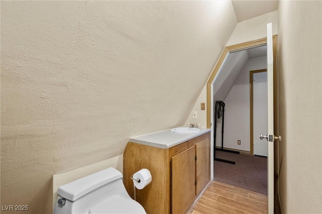 bathroom featuring hardwood / wood-style flooring, vanity, toilet, and lofted ceiling