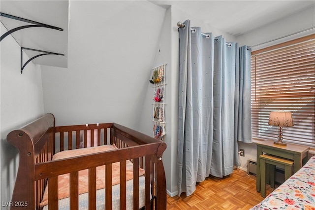 bedroom featuring a crib, light parquet flooring, and a baseboard heating unit