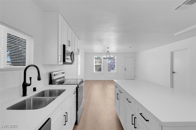 kitchen with appliances with stainless steel finishes, sink, an inviting chandelier, white cabinetry, and hanging light fixtures