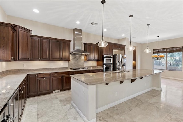 kitchen featuring visible vents, light stone countertops, stainless steel appliances, wall chimney range hood, and a sink