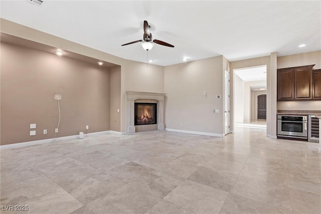 unfurnished living room with recessed lighting, a ceiling fan, a glass covered fireplace, beverage cooler, and baseboards